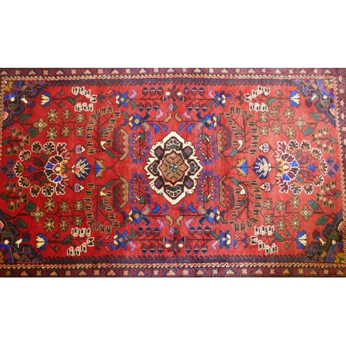 1213 - An oriental Hamadan wool carpet with medallion design on a red field, 82