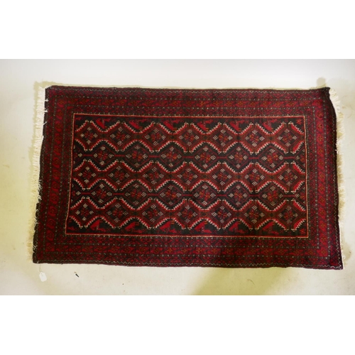 1215 - A Belouch wool rug, geometric designs on a plum red field, 62