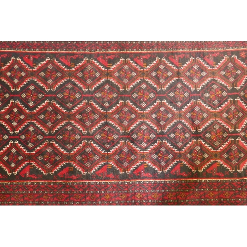 1215 - A Belouch wool rug, geometric designs on a plum red field, 62