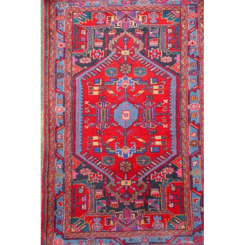 1170 - A Persian red ground wool rug with a multicolour geometric medallion design, 33