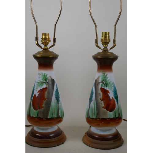 16 - A pair of opaline glass table lamps with hand painted decoration of red squirrels amongst pine trees... 