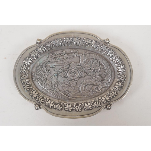 28 - A Chinese white metal trinket dish of lobed form, with raised dragon and phoenix decoration, impress... 