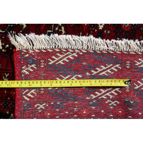 1176 - A deep red ground Persian Bokhara carpet, 184cm x 280cm