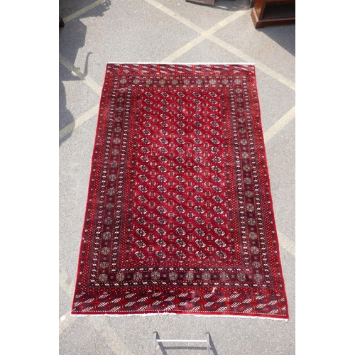 1176 - A deep red ground Persian Bokhara carpet, 184cm x 280cm