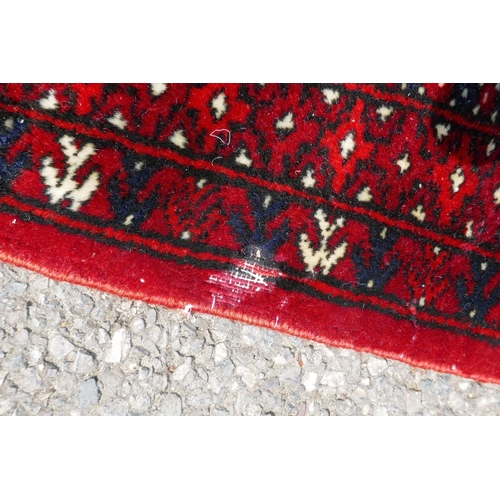 1176 - A deep red ground Persian Bokhara carpet, 184cm x 280cm