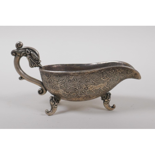 45 - A Chinese white metal libation cup on tripod supports, with dragon head shaped handle and mythical c... 