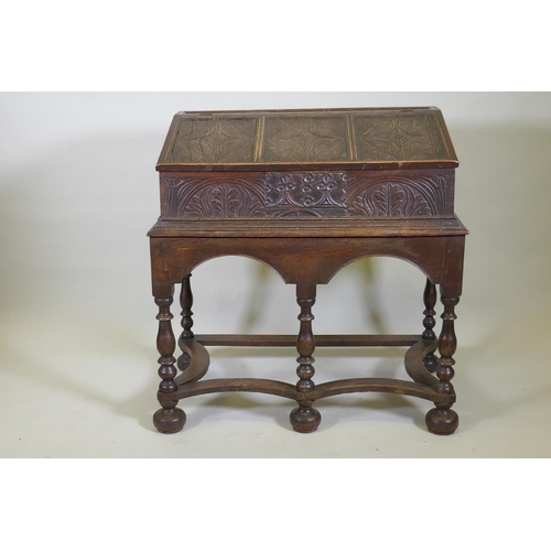 1023 - A carved oak bible box on stand, with triple panel fall front, the stand raised on baluster turned s... 