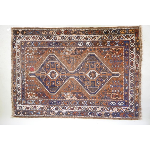 1076 - An antique terracotta ground Persian wool village rug, with a twin geometric medallion design, AF, 1... 