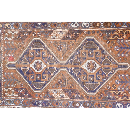 1076 - An antique terracotta ground Persian wool village rug, with a twin geometric medallion design, AF, 1... 