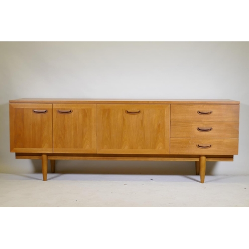 1099 - A mid century teak sideboard with two cupboards and three drawers flanking a central fall front, rai... 