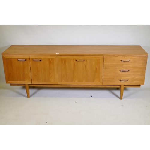 1099 - A mid century teak sideboard with two cupboards and three drawers flanking a central fall front, rai... 