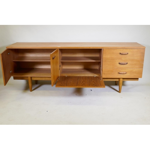 1099 - A mid century teak sideboard with two cupboards and three drawers flanking a central fall front, rai... 