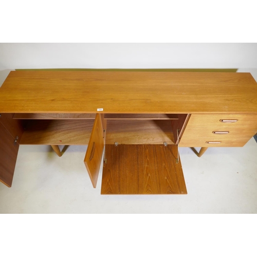 1099 - A mid century teak sideboard with two cupboards and three drawers flanking a central fall front, rai... 