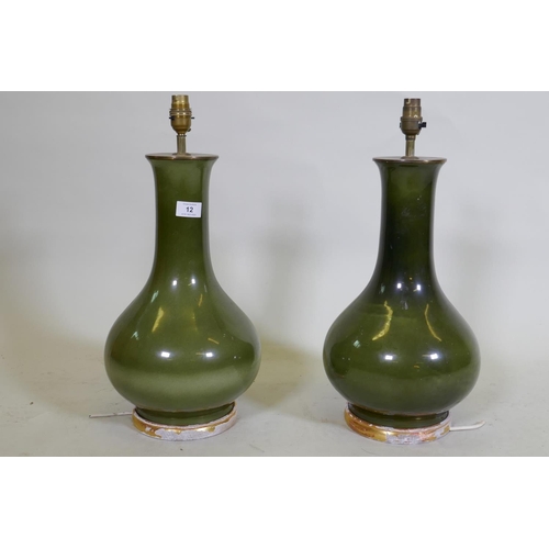 12 - A pair of green glazed ceramic table lamps with brass mounts, mounted on distressed giltwood bases, ... 