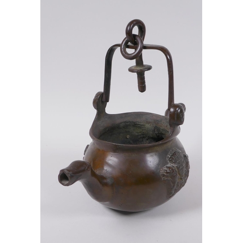 137 - A solid bronze double spouted hanging tea pot with heraldic decoration, 29cm long