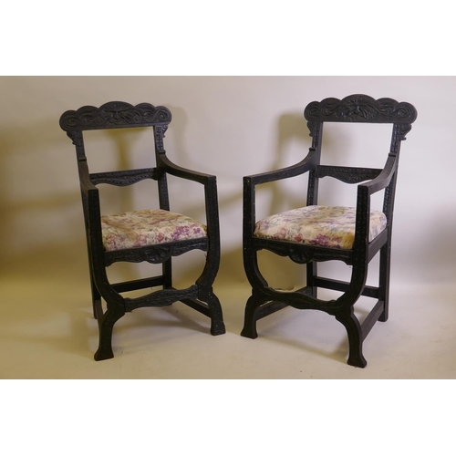 1021 - A pair of C19th ebonised X frame chairs with carved Green Man decoration and drop in seats