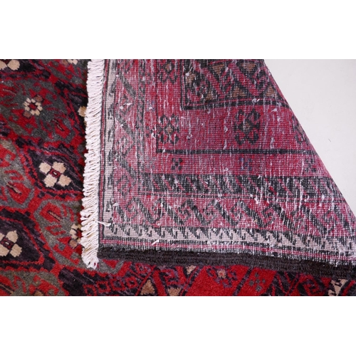 1087 - A full pile hand woven red ground carpet with a geometric floral design, 268 x 130cm