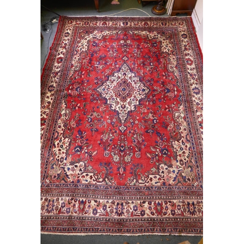 1099 - A Persian full pile red ground hand woven Sarouk village carpet with a floral medallion pattern and ... 