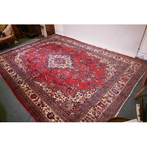 1099 - A Persian full pile red ground hand woven Sarouk village carpet with a floral medallion pattern and ... 