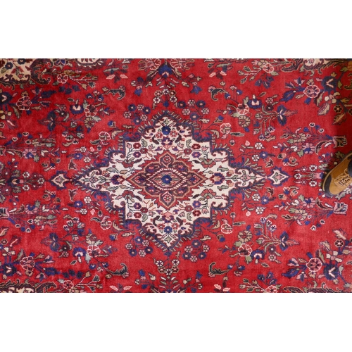 1099 - A Persian full pile red ground hand woven Sarouk village carpet with a floral medallion pattern and ... 