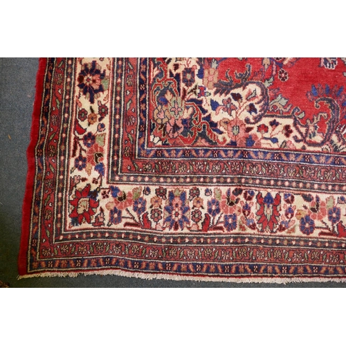 1099 - A Persian full pile red ground hand woven Sarouk village carpet with a floral medallion pattern and ... 