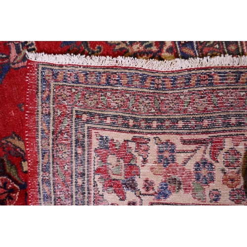 1099 - A Persian full pile red ground hand woven Sarouk village carpet with a floral medallion pattern and ... 