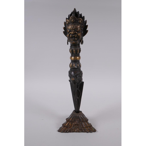 231 - A Tibetan bronze ceremonial phurba and stand, with a wrathful deity mask to handle, 33cm high