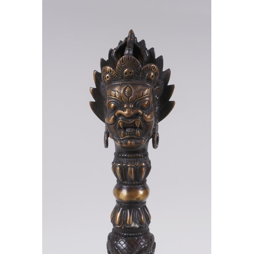 231 - A Tibetan bronze ceremonial phurba and stand, with a wrathful deity mask to handle, 33cm high