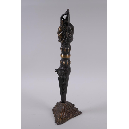 231 - A Tibetan bronze ceremonial phurba and stand, with a wrathful deity mask to handle, 33cm high