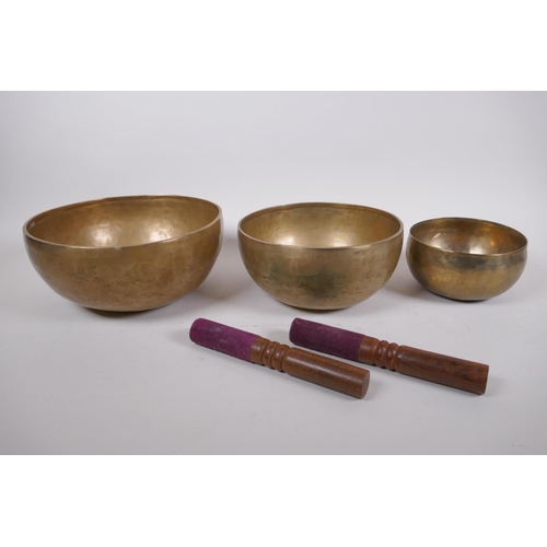 276 - Three Tibetan graduated polished bronze singing bowls, with hammered finish and two wood hammers, la... 