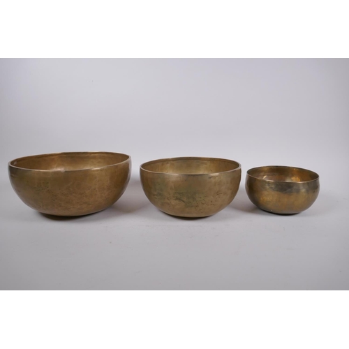 276 - Three Tibetan graduated polished bronze singing bowls, with hammered finish and two wood hammers, la... 