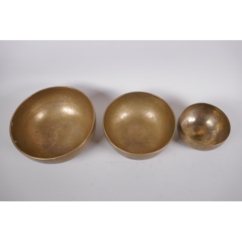 276 - Three Tibetan graduated polished bronze singing bowls, with hammered finish and two wood hammers, la... 