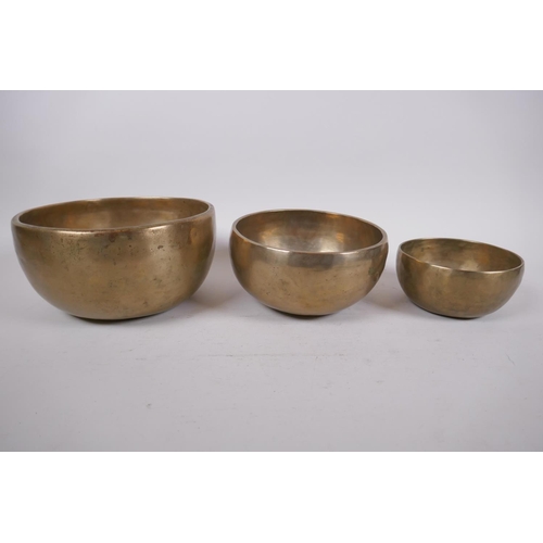 277 - Three Tibetan graduated polished bronze singing bowls with hammered finish, and two wood hammers, la... 