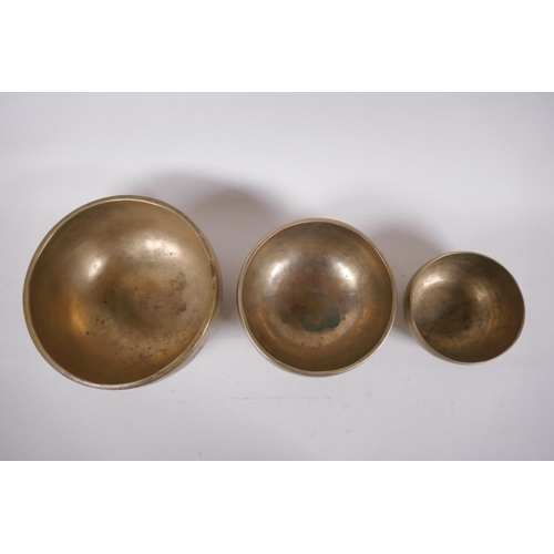 277 - Three Tibetan graduated polished bronze singing bowls with hammered finish, and two wood hammers, la... 