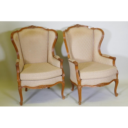 1018 - A pair of Louis XV style walnut wingback arm chairs with carved detail