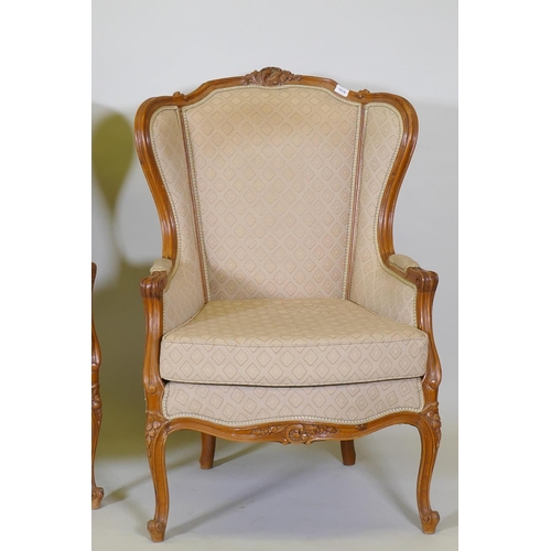 1018 - A pair of Louis XV style walnut wingback arm chairs with carved detail