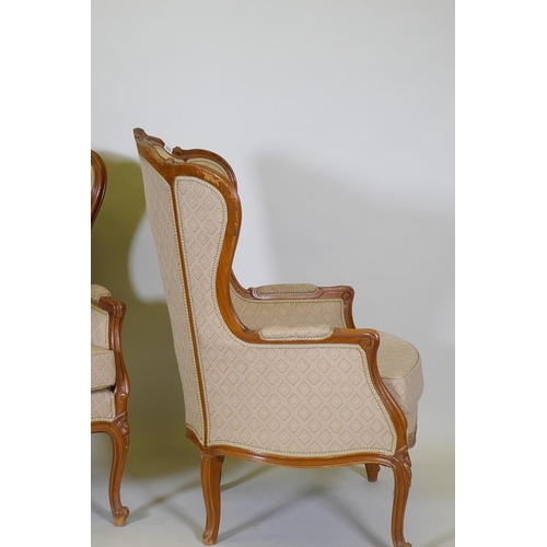 1018 - A pair of Louis XV style walnut wingback arm chairs with carved detail