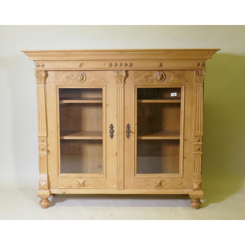 1100 - A C19th continental pine bookcase with two glazed door with applied fluted columns and lion mask dec... 