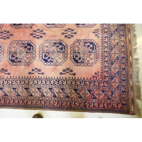 1130 - A vintage faded red hand woven wool Bokhara carpet with geometric designs, 130 x 210cm