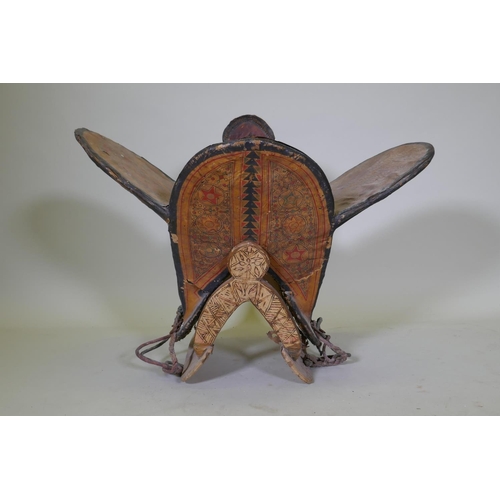 154 - A hand painted animal hide, wood and leather camel saddle with metal mounts and stand, probably of t... 