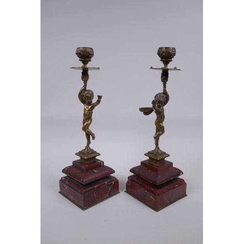 17 - A pair of Victorian bronze candlesticks in the form of a winged putti, on red marble bases, 28cm hig... 