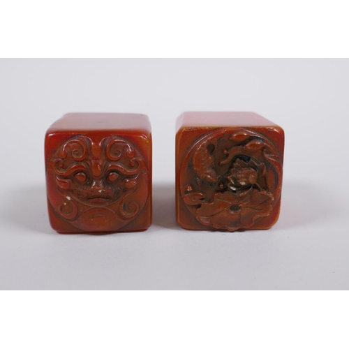 183 - A pair of Chinese amber soapstone seals with dragon mask and lotus pad decoration, 3 x 3cm, 4cm high