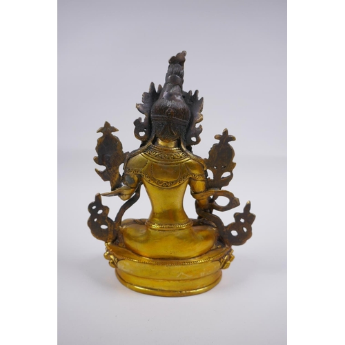 210 - A Tibetan gilt bronze figure of a female deity seated on a lotus flower, impressed double vajra mark... 