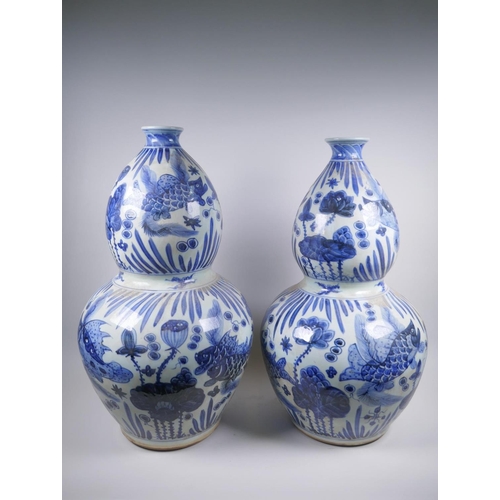 56 - A near pair of Chinese blue and white porcelain double gourd vases decorated with carp in a lotus po... 