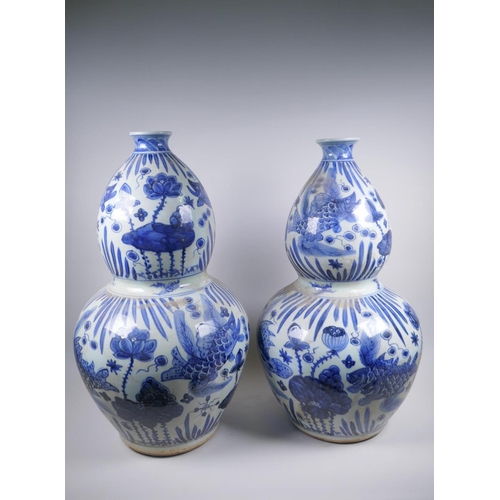 56 - A near pair of Chinese blue and white porcelain double gourd vases decorated with carp in a lotus po... 