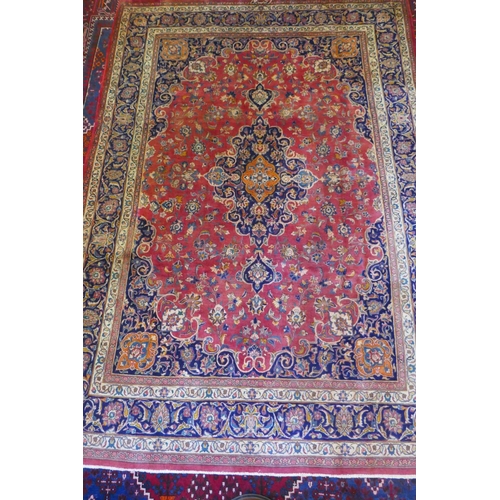 1020 - A washed red ground Persian Mashad carpet with traditional floral medallion design, signed by the we... 