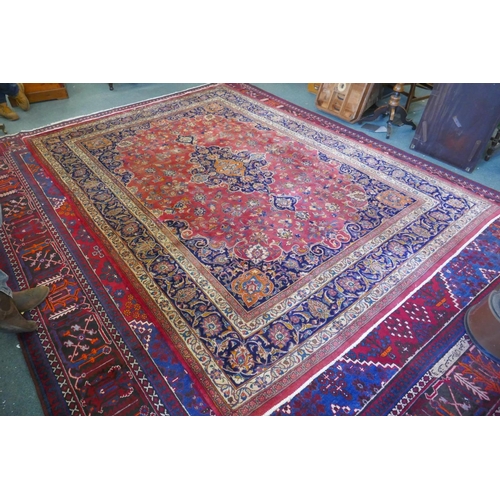 1020 - A washed red ground Persian Mashad carpet with traditional floral medallion design, signed by the we... 