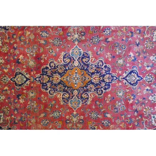 1020 - A washed red ground Persian Mashad carpet with traditional floral medallion design, signed by the we... 