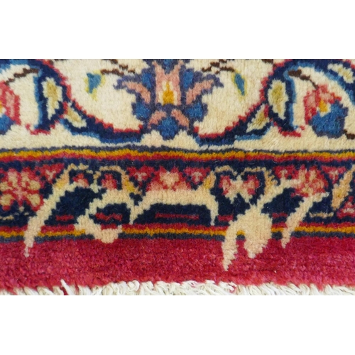 1020 - A washed red ground Persian Mashad carpet with traditional floral medallion design, signed by the we... 