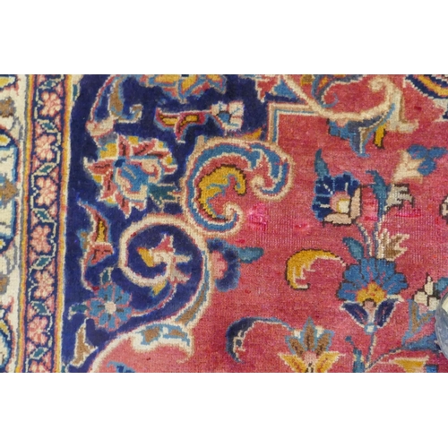 1020 - A washed red ground Persian Mashad carpet with traditional floral medallion design, signed by the we... 